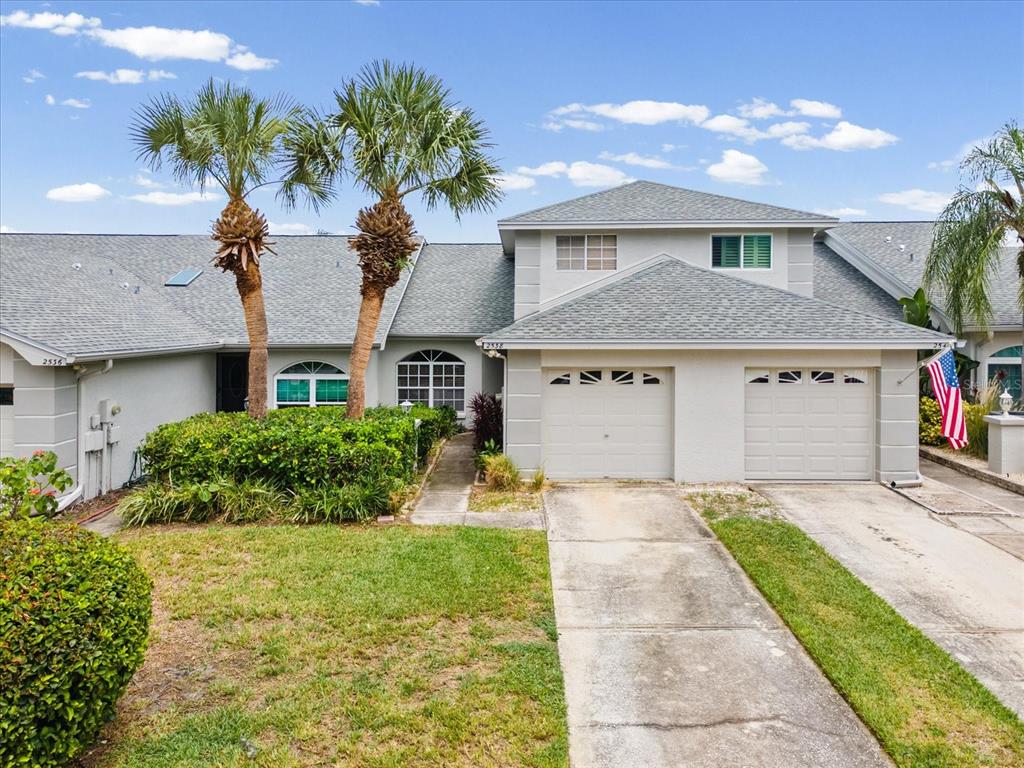 A two-story gray townhouse features a two-car garage, palm trees, and a landscaped front yard — 2538 W BROOK LANE, CLEARWATER, FL