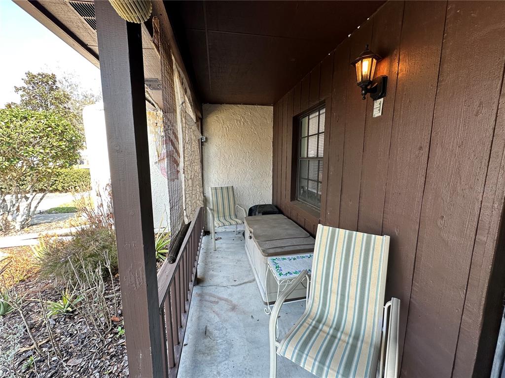 A covered porch features brown wood siding, a concrete floor, and two striped chairs — 913 MICHIGAN AVENUE, ST CLOUD, FL