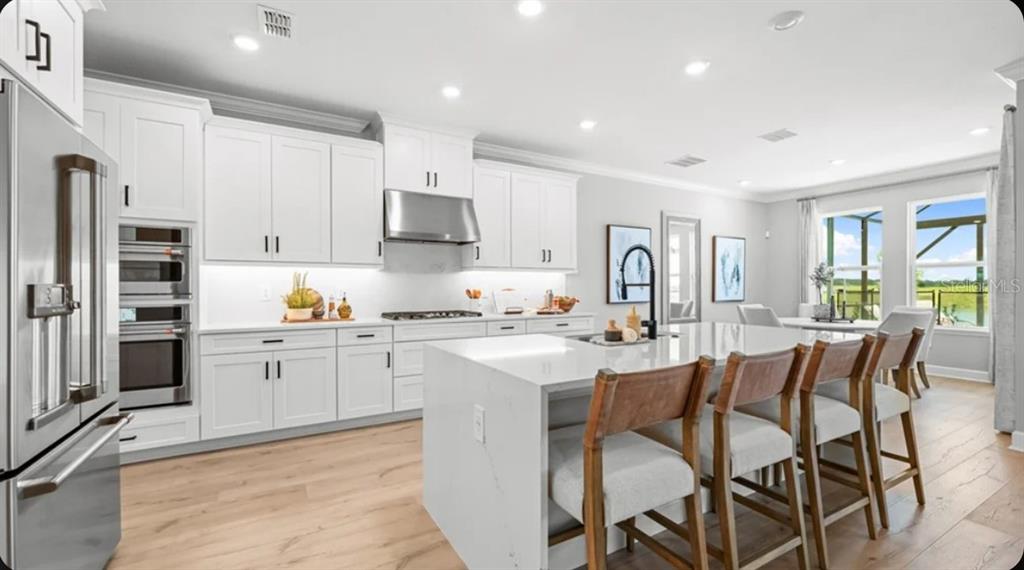 A modern kitchen features white cabinetry, a large quartz island with seating, and stainless appliances — 5372 GUNWALE DRIVE, COCOA, FL