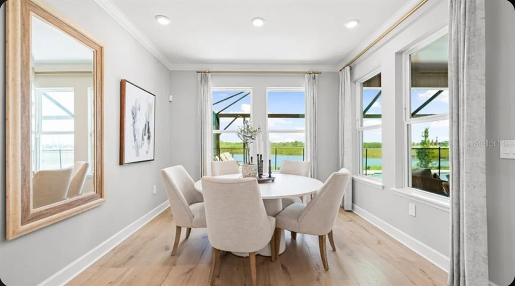 A dining room with a round table, upholstered chairs, light wood floors, and large windows — 5372 GUNWALE DRIVE, COCOA, FL