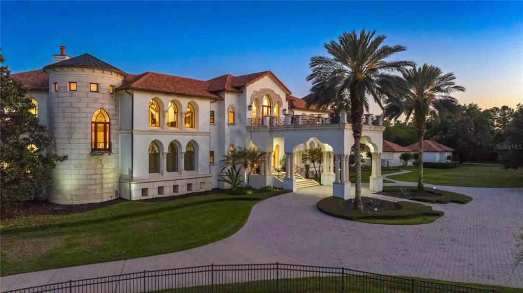 A large Mediterranean-style mansion with a stone turret, arched windows, and a circular driveway — 5603 MARLEON DRIVE, WINDERMERE, FL