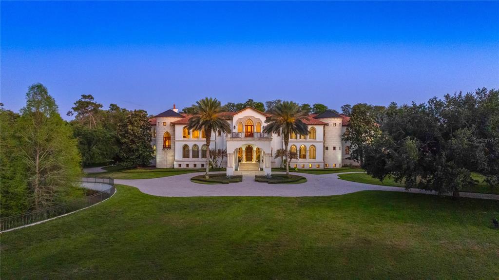 An aerial view of a large, white Mediterranean-style mansion with a circular driveway and palms — 5603 MARLEON DRIVE, WINDERMERE, FL