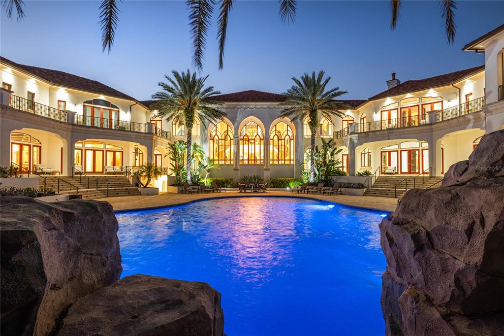 A large swimming pool sits in the courtyard of a multi-story Mediterranean-style mansion at dusk — 5603 MARLEON DRIVE, WINDERMERE, FL