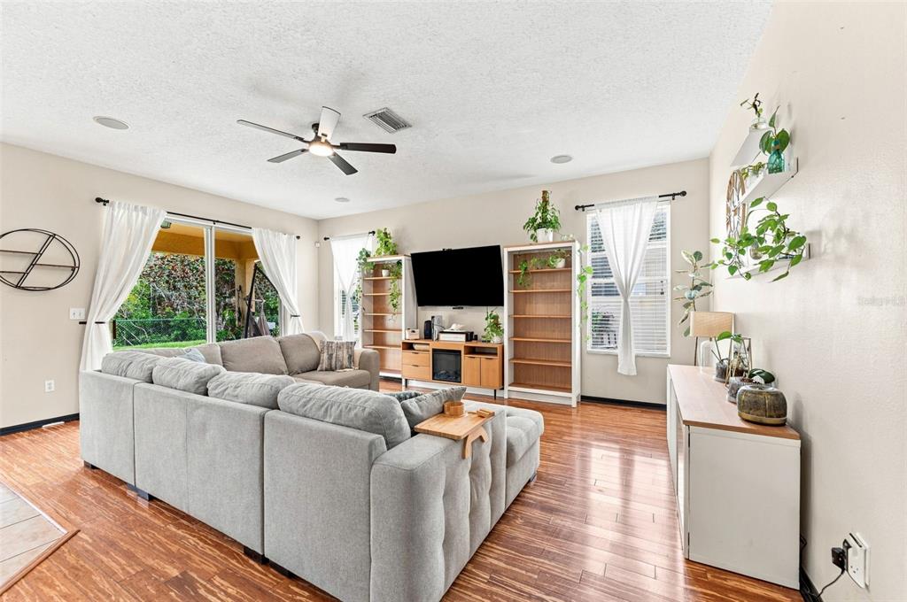 A living room features a grey sectional sofa, wood flooring, and a wall-mounted television — 15731 CEDAR ELM TERRACE, LAND O LAKES, FL