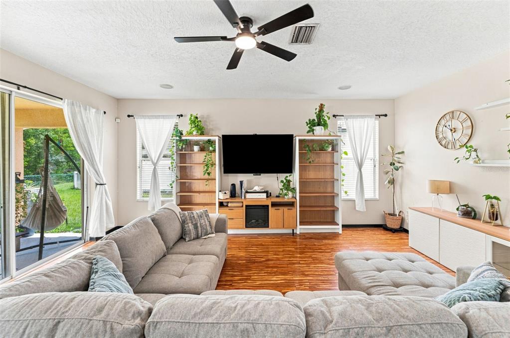 A living room features a large sectional sofa, wood flooring, a television, and shelving units — 15731 CEDAR ELM TERRACE, LAND O LAKES, FL