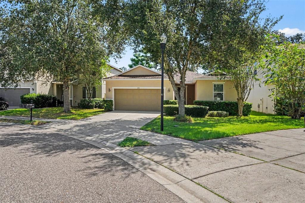 A single-story house with a tan exterior, a two-car garage, and mature trees in front — 1102 CANYON OAKS DRIVE, BRANDON, FL