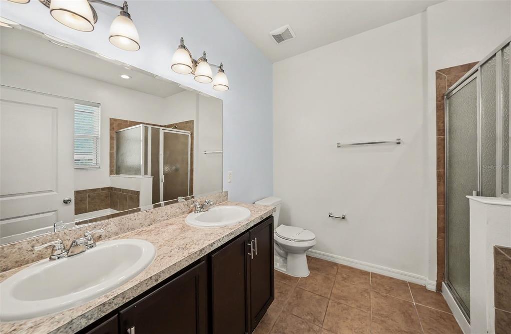 A bathroom features a double vanity with dark cabinets, granite countertops, and a glass shower — 1102 CANYON OAKS DRIVE, BRANDON, FL