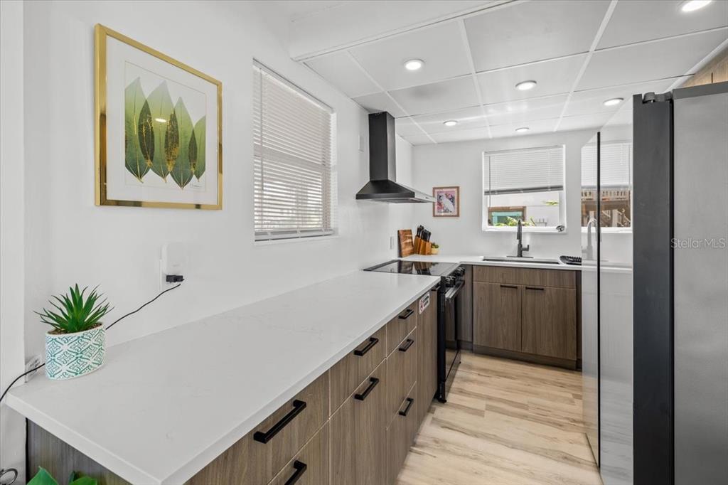 A modern kitchen features wood-grain cabinets, white countertops, a black range hood, and recessed lighting — 4009 CASA COURT, HERNANDO BEACH, FL