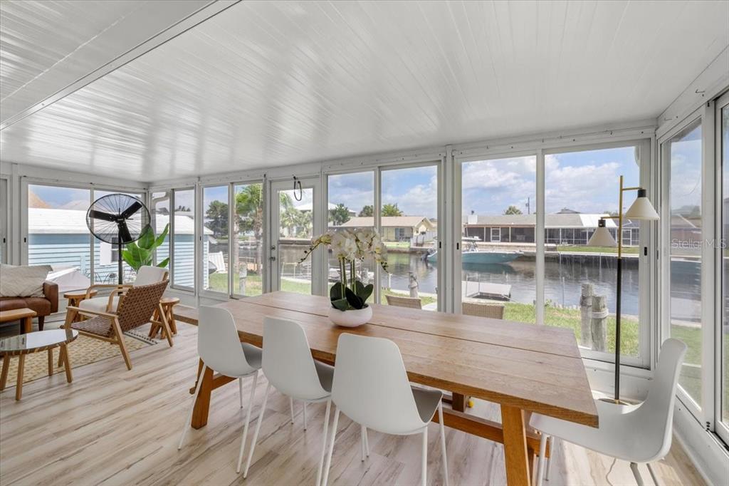A sunroom features a wooden dining table, white chairs, and large windows overlooking a canal — 4009 CASA COURT, HERNANDO BEACH, FL