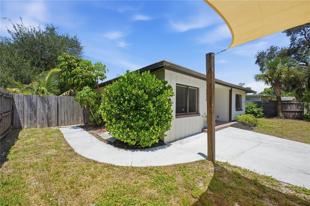 A small house exterior features a concrete patio, a large green bush, and a shade sail — 4925 REMINGTON DRIVE, SARASOTA, FL