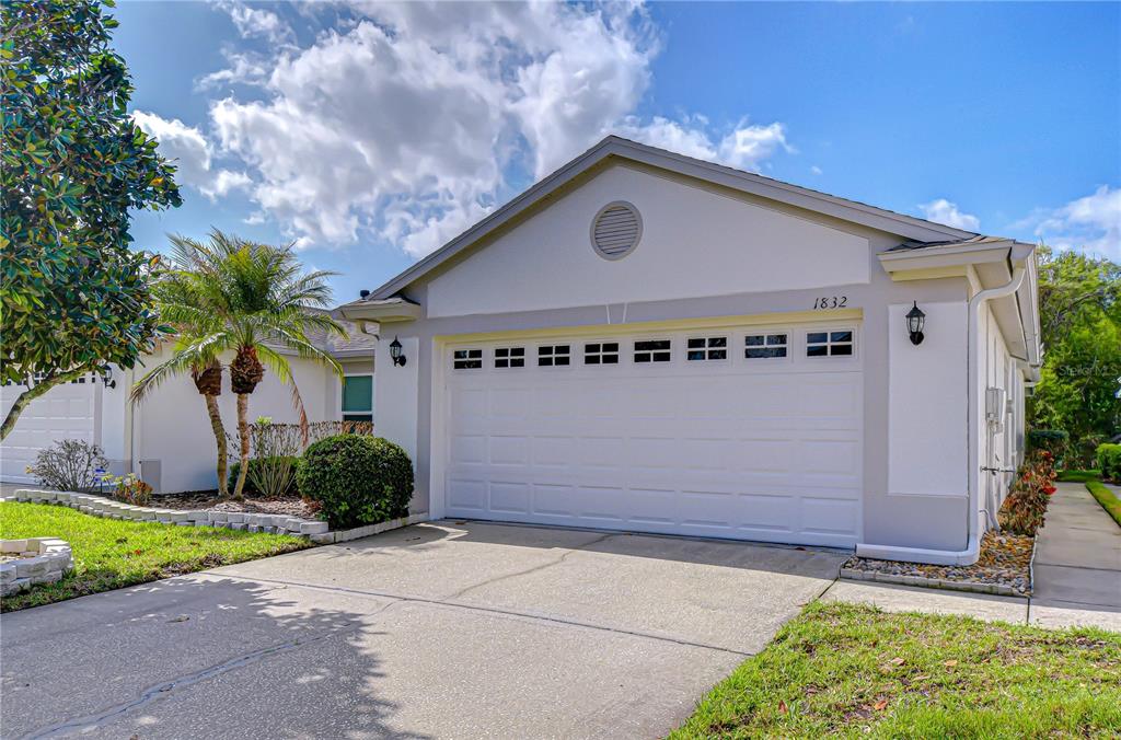 A single-story house exterior features a two-car garage, a concrete driveway, and a palm tree — 1832 SASSAFRAS DRIVE, WESLEY CHAPEL, FL