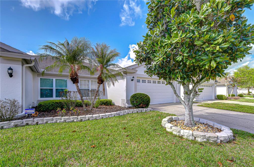 A single-story house exterior features a two-car garage, palm trees, and a landscaped front yard — 1832 SASSAFRAS DRIVE, WESLEY CHAPEL, FL