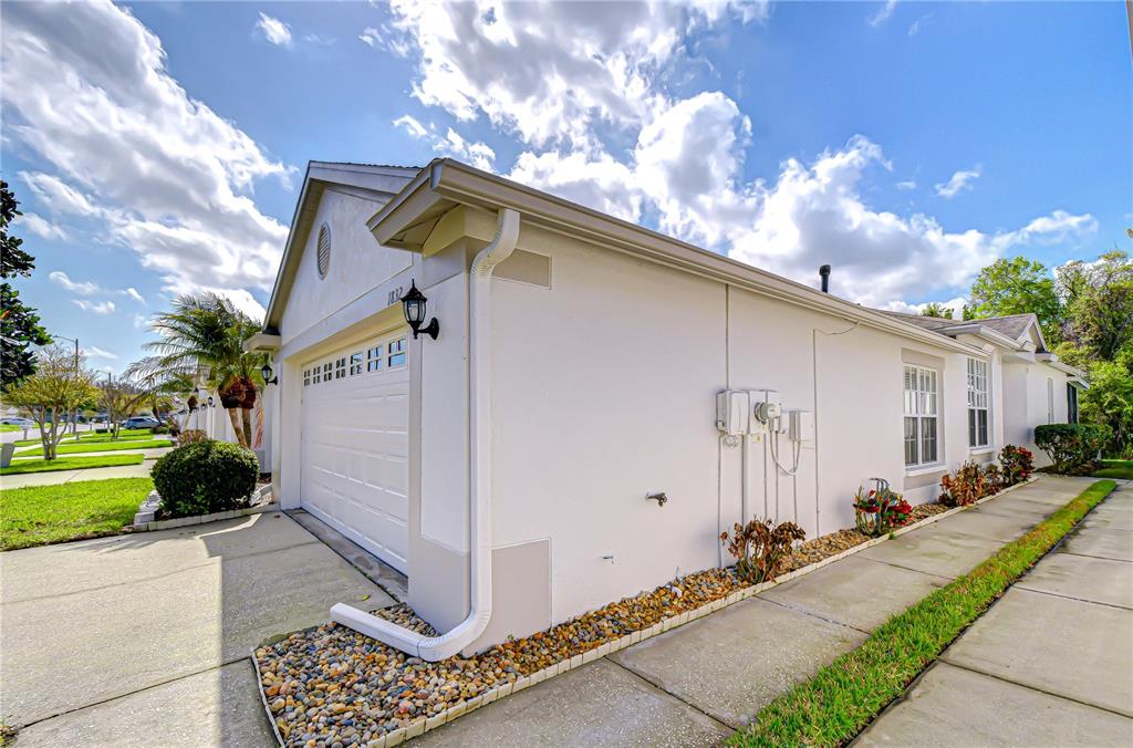 The exterior of a light-colored house features a garage, a concrete driveway, and landscaping — 1832 SASSAFRAS DRIVE, WESLEY CHAPEL, FL