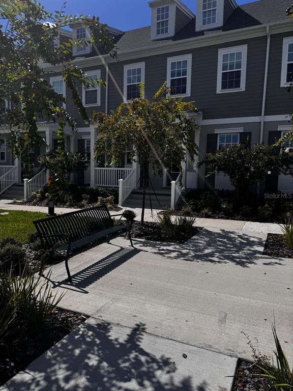 A black metal bench sits on a concrete walkway in front of gray townhouses — 2386 CELEBRATION BOULEVARD, CELEBRATION, FL