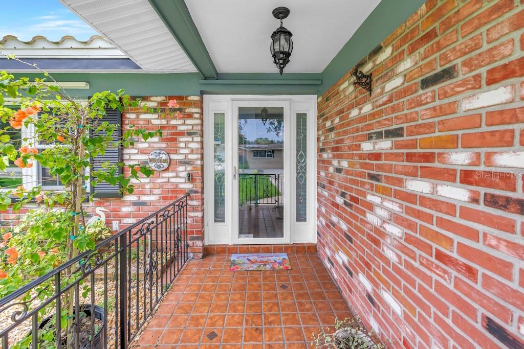 A brick-walled front porch features a glass storm door, tile flooring, and black metal railings — 731 OBERLIN DRIVE, CLEARWATER, FL