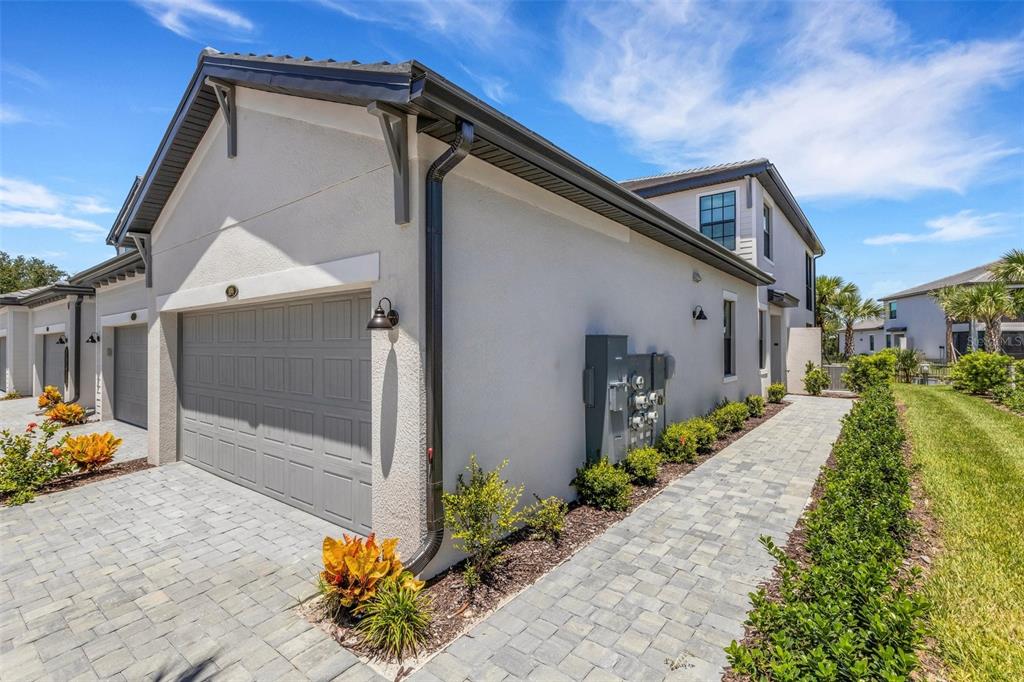 A side view of a beige townhouse with a gray garage door and paver walkway — 5624 SUMMIT POINTE CIRCLE UNIT 104, BRADENTON, FL