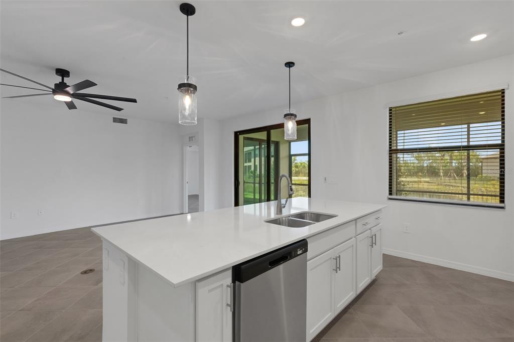 A kitchen island with a stainless steel dishwasher and sink sits in a bright room — 5624 SUMMIT POINTE CIRCLE UNIT 104, BRADENTON, FL