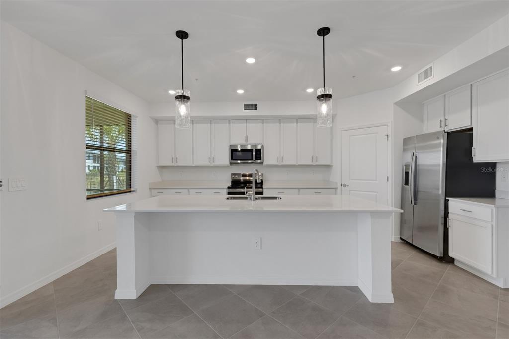 A modern kitchen features white cabinetry, stainless steel appliances, a large island, and tile flooring — 5624 SUMMIT POINTE CIRCLE UNIT 104, BRADENTON, FL