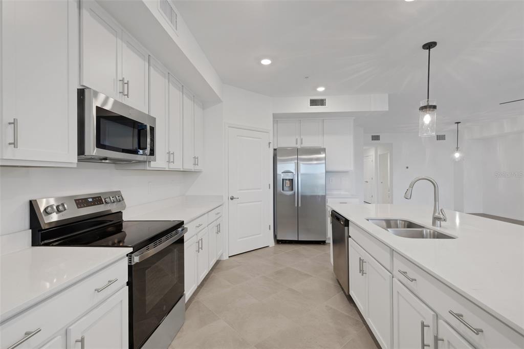 A modern kitchen features white cabinets, stainless steel appliances, quartz countertops, and light tile flooring — 5624 SUMMIT POINTE CIRCLE UNIT 104, BRADENTON, FL