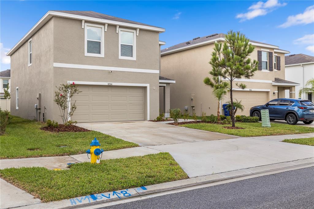 A two-story suburban house with a tan stucco exterior and a two-car garage — 9294 FORGE BREEZE LOOP, WESLEY CHAPEL, FL