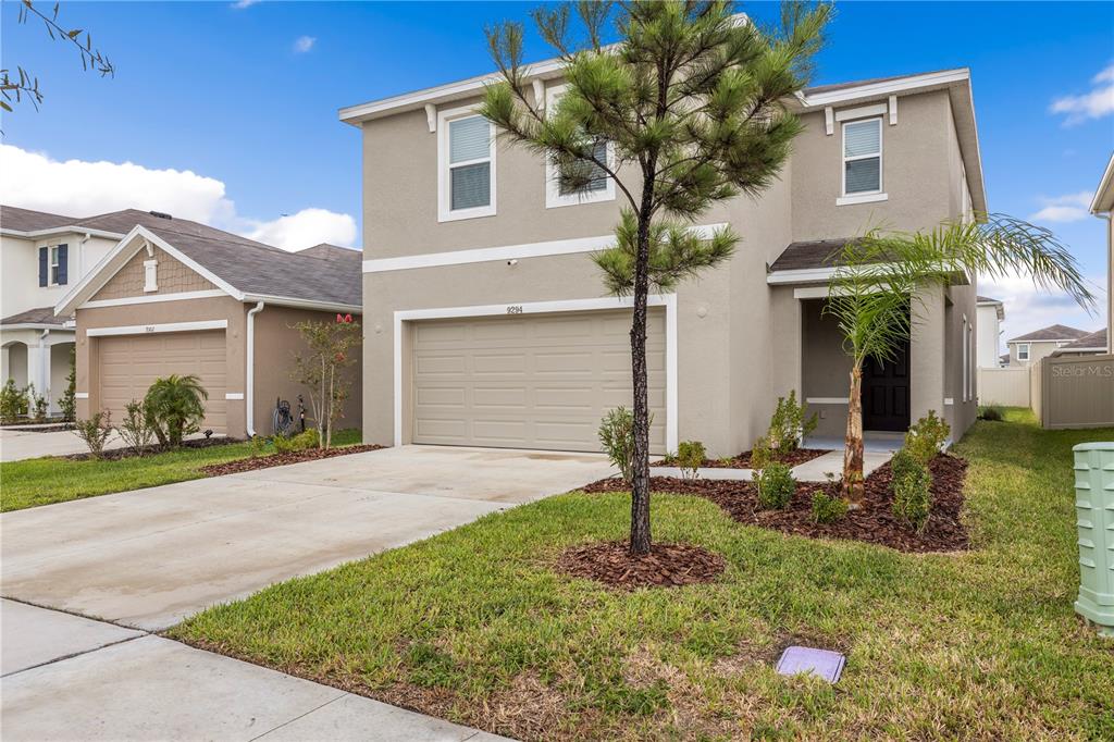 A two-story suburban house with a beige stucco exterior, a two-car garage, and a lawn — 9294 FORGE BREEZE LOOP, WESLEY CHAPEL, FL