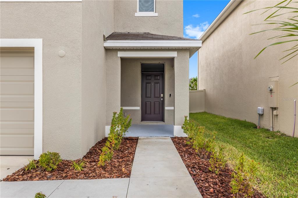 A concrete walkway leads to the front door of a tan house with a garage — 9294 FORGE BREEZE LOOP, WESLEY CHAPEL, FL