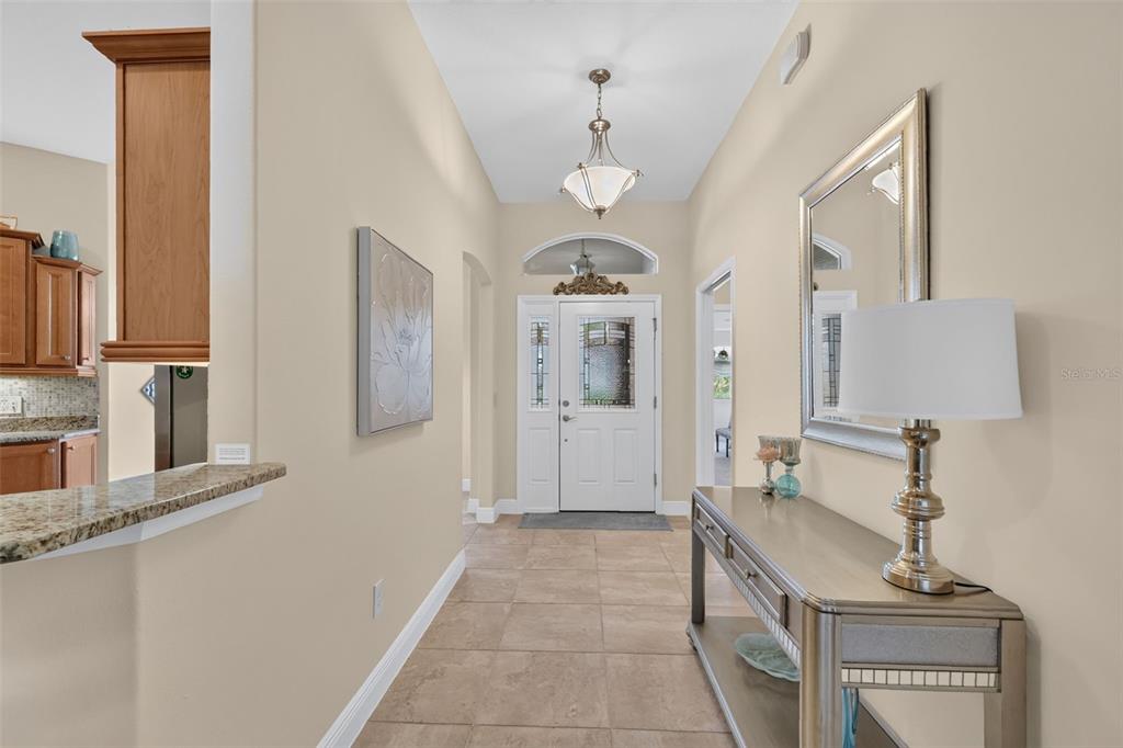 A tiled entryway features a console table, a mirror, and a white front door — 1473 QUARTER TERRACE, THE VILLAGES, FL