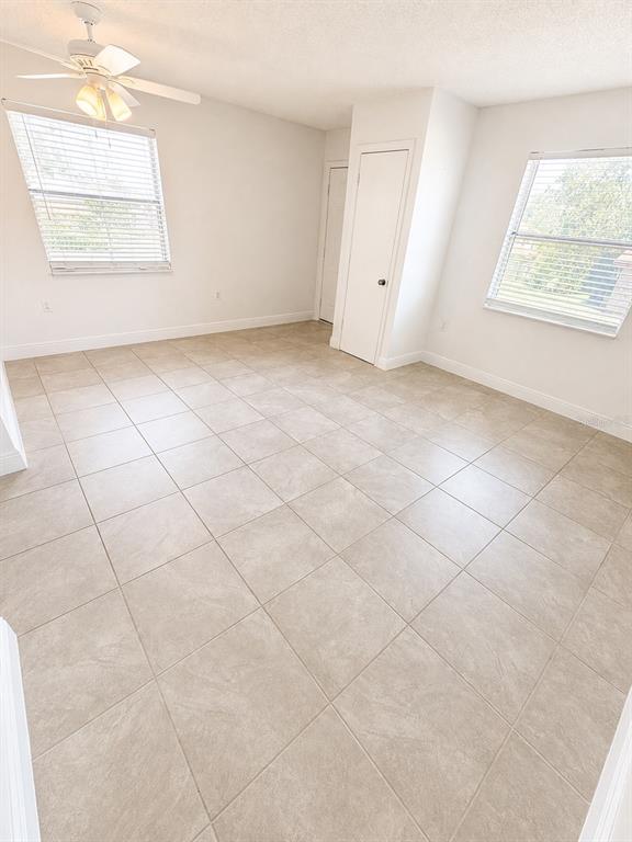 An empty bedroom features light-colored tile flooring, a ceiling fan, and two windows with blinds — 1183-1183 BENTLEY ROAD UNIT 4, LEESBURG, FL