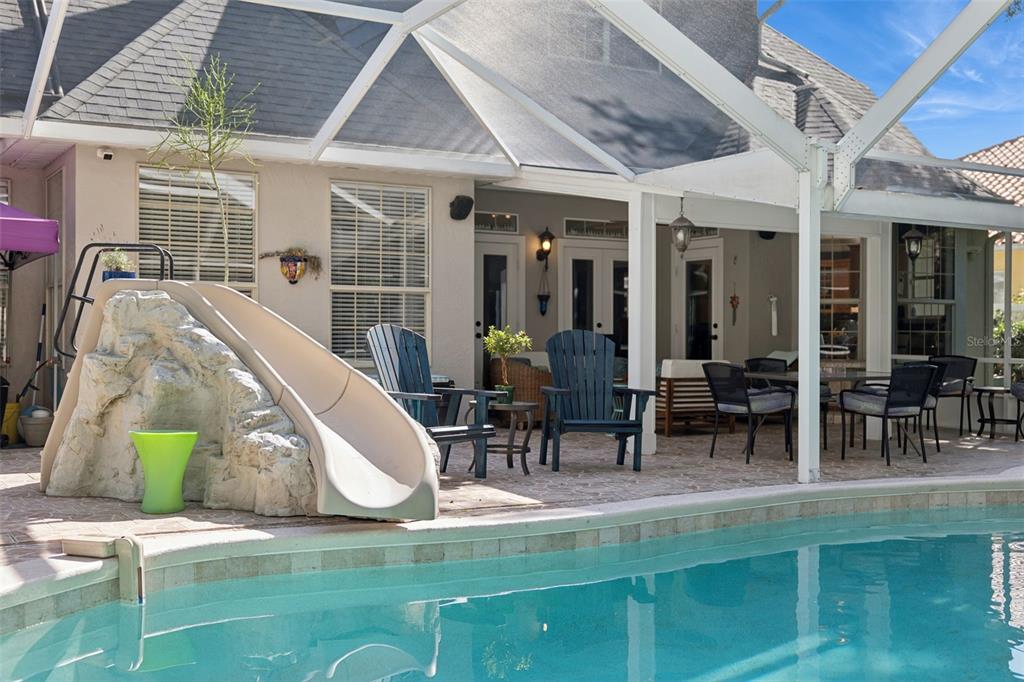 A screened-in patio features a pool slide, outdoor seating, and a view of the pool — 11 FOXHUNTER FLAT, ORMOND BEACH, FL