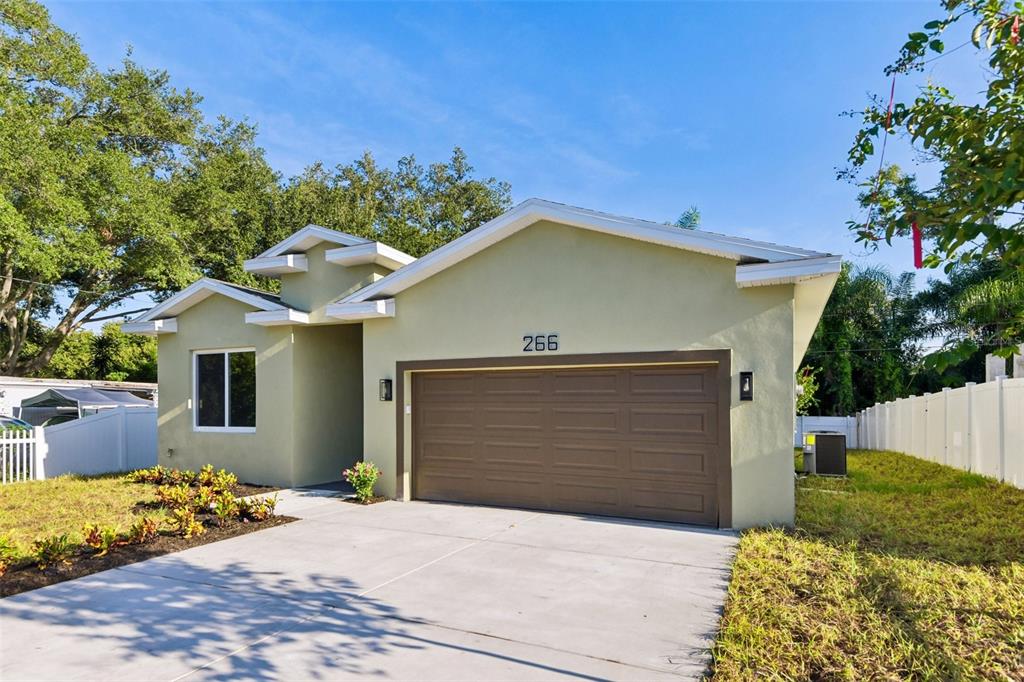 A single-story house with a light green exterior, a brown garage door, and a concrete driveway — 266 PLATON AVENUE, DUNEDIN, FL