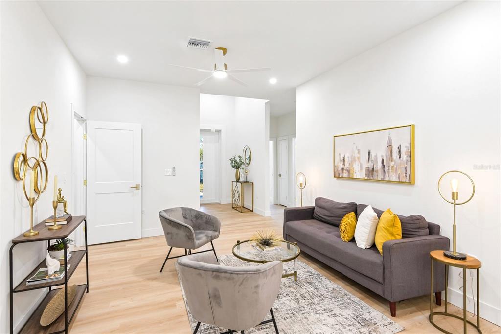 A modern living room features a grey sofa, two velvet chairs, and gold-toned accent decor — 266 PLATON AVENUE, DUNEDIN, FL