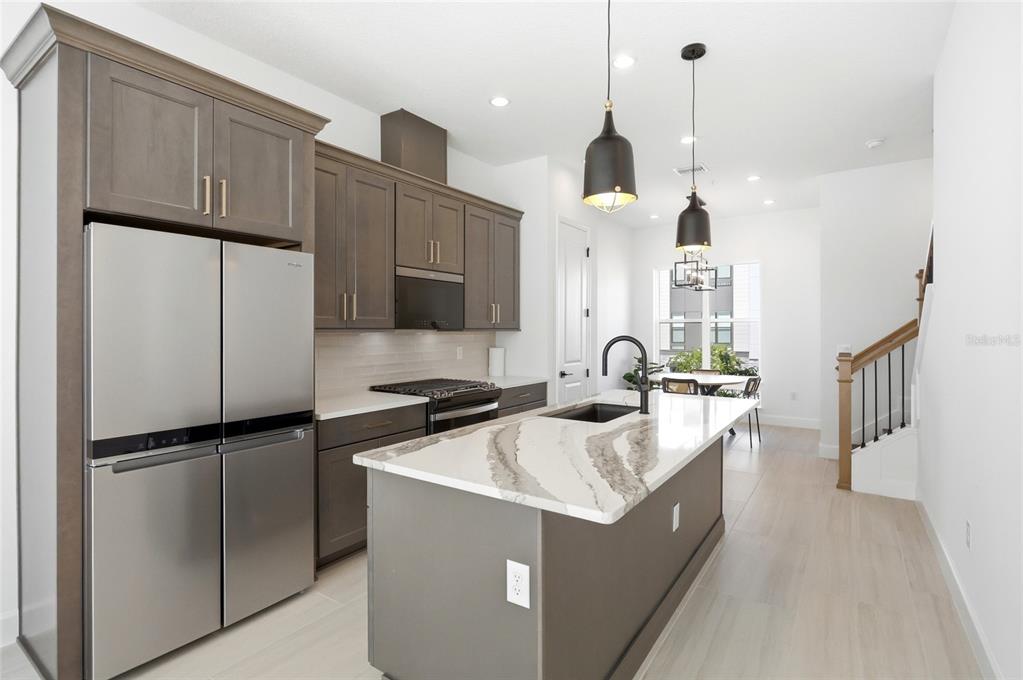 A modern kitchen features dark cabinetry, a marble-topped island, stainless steel appliances, and light flooring — 2130 WHITNEY MARSH ALLEY, ORLANDO, FL