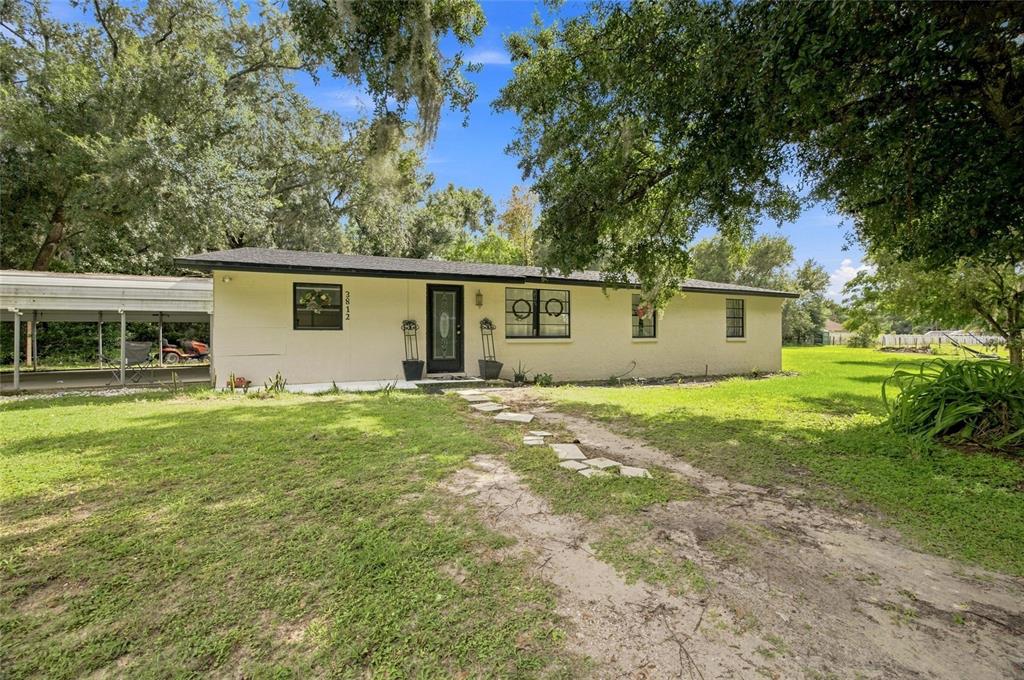 A single-story house with a light-colored stucco exterior, a black roof, and a carport — 3812 REVEREND DAR DAR DRIVE, PLANT CITY, FL