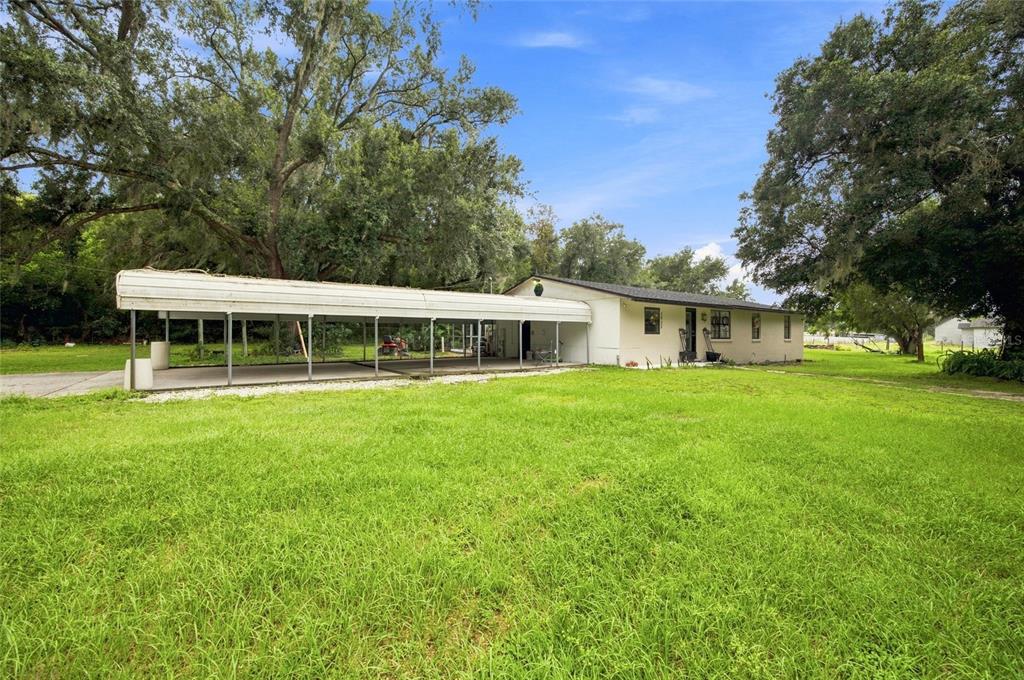 A single-story house with a large attached metal carport sits on a grassy lot — 3812 REVEREND DAR DAR DRIVE, PLANT CITY, FL