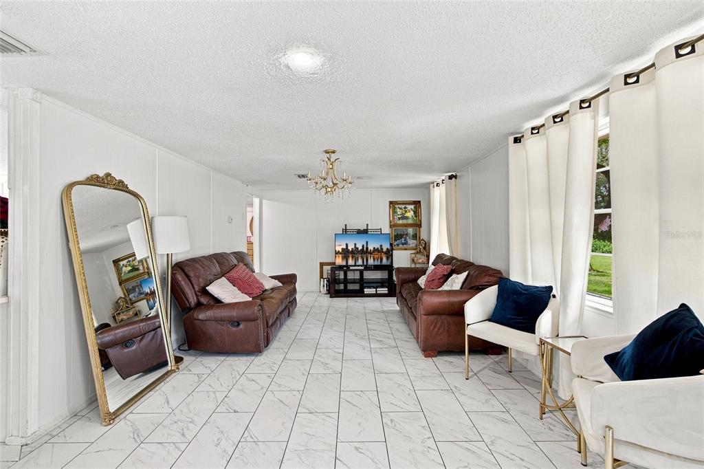 A living room features white marble-look tile floors, two brown leather sofas, and a large mirror — 3812 REVEREND DAR DAR DRIVE, PLANT CITY, FL