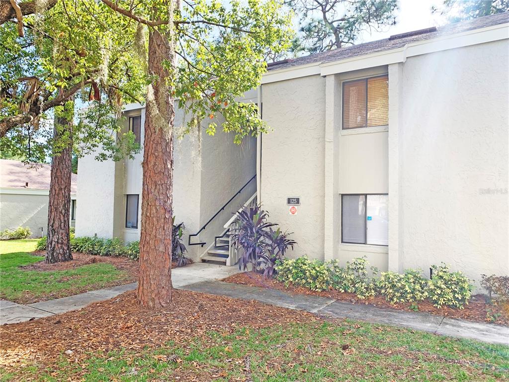 A two-story apartment building exterior features a concrete staircase leading to an upper-level entrance — 125 SPRINGWOOD CIRCLE UNIT D, LONGWOOD, FL
