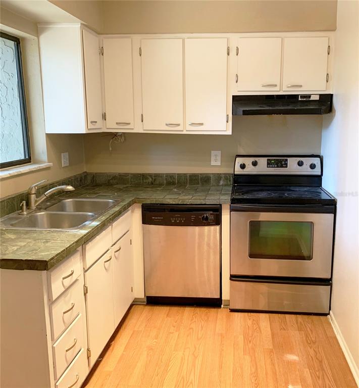 A kitchen features white cabinets, green tile countertops, stainless steel appliances, and wood-look flooring — 125 SPRINGWOOD CIRCLE UNIT D, LONGWOOD, FL