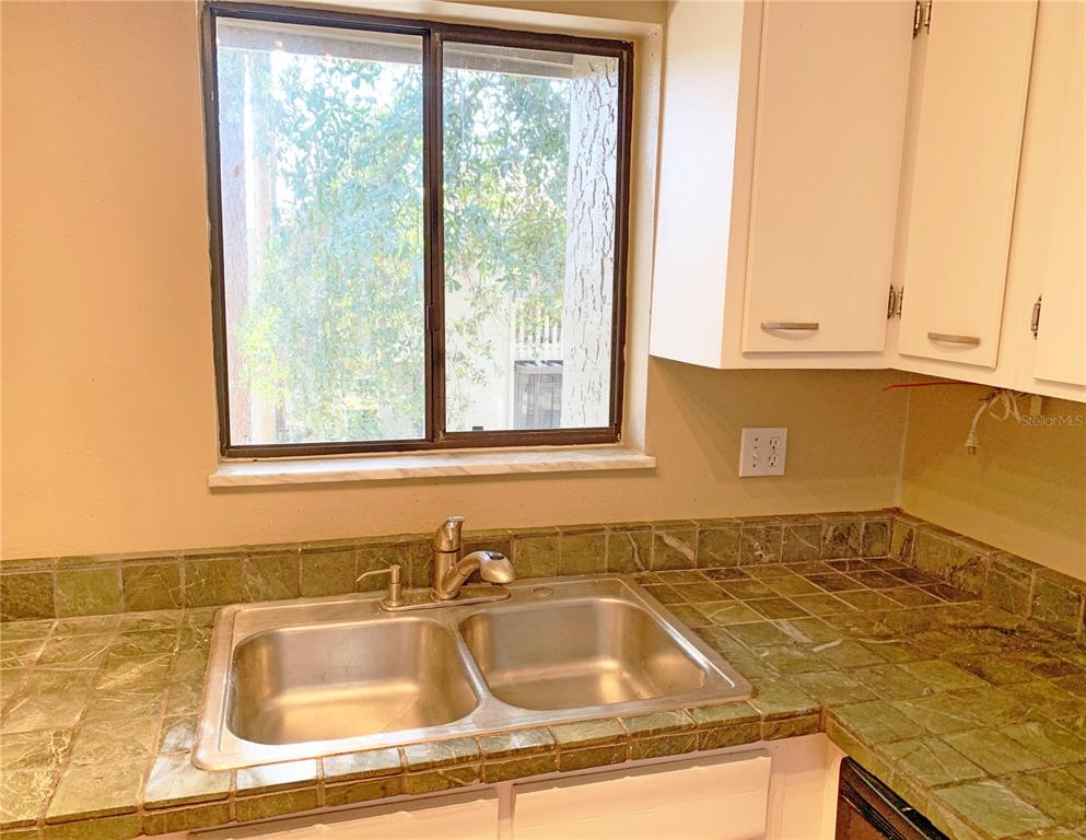 A kitchen sink with a metal faucet sits in a green tiled countertop by a window — 125 SPRINGWOOD CIRCLE UNIT D, LONGWOOD, FL