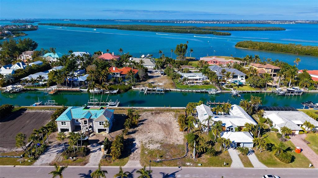 An aerial view shows waterfront homes, a vacant lot, and a canal leading to a bay — 721 EMERALD HARBOR DRIVE, LONGBOAT KEY, FL