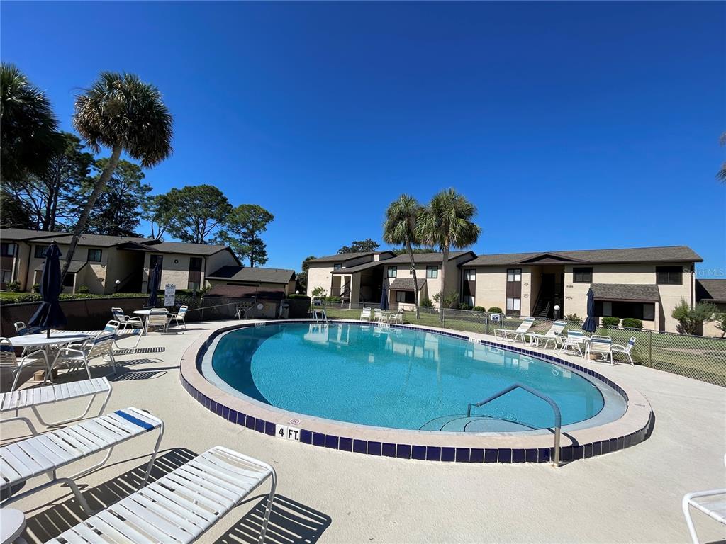 An outdoor swimming pool surrounded by lounge chairs and apartment buildings under a clear sky — 647 MIDWAY DRIVE UNIT B, OCALA, FL