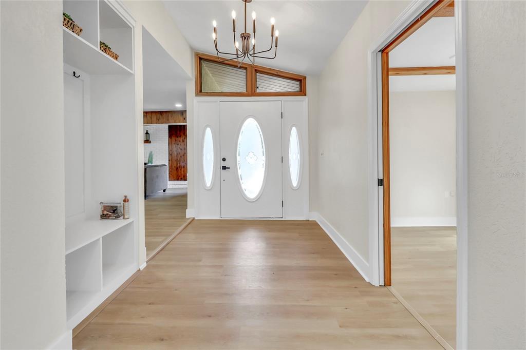 A bright entryway features light wood flooring, a white front door, and a modern chandelier — 16123 E LAKE BURRELL DRIVE, LUTZ, FL