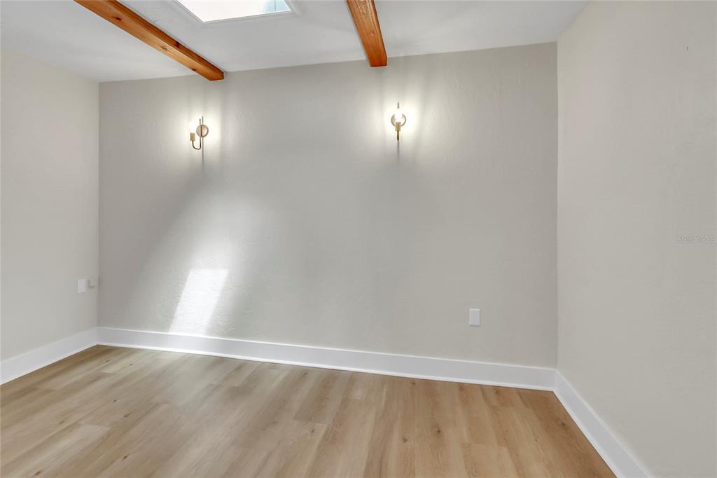 An empty room features light wood flooring, white walls, two wall sconces, and exposed ceiling beams — 16123 E LAKE BURRELL DRIVE, LUTZ, FL