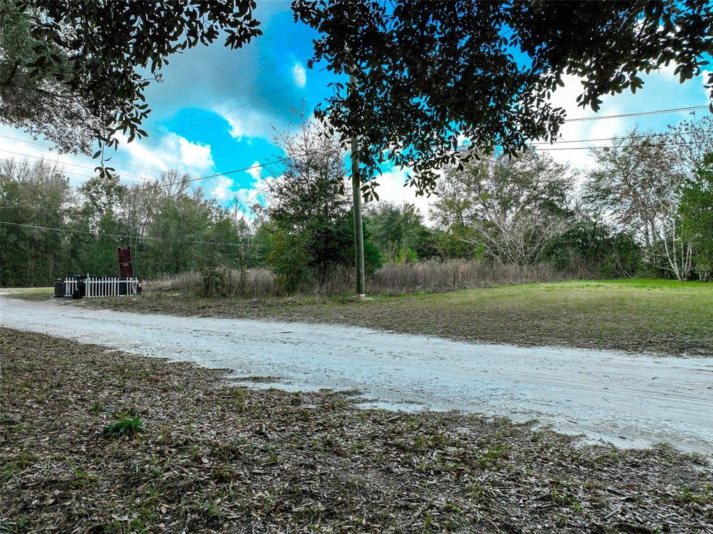 A dirt road leads past a small white fence toward a wooded, grassy lot — 106 NW FAT CAT COURT, LAKE CITY, FL