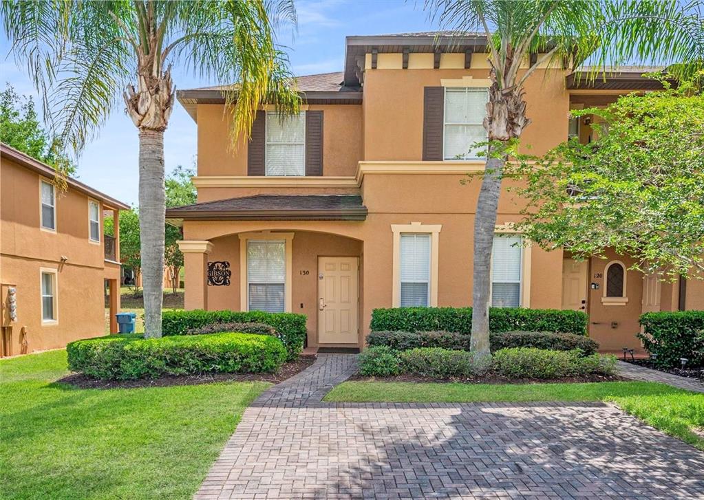 A two-story tan stucco townhouse with a brick paver walkway and palm trees in front — 130 PALERMO STREET, DAVENPORT, FL