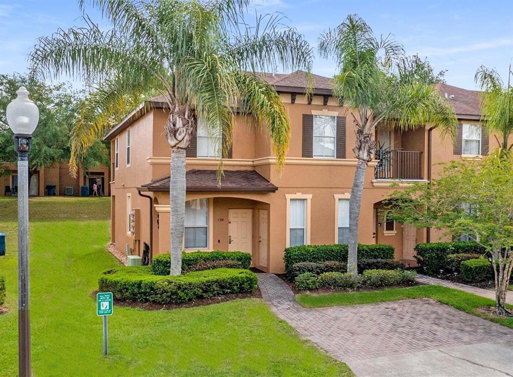 A two-story tan stucco townhouse with a brick paver walkway and two palm trees — 130 PALERMO STREET, DAVENPORT, FL