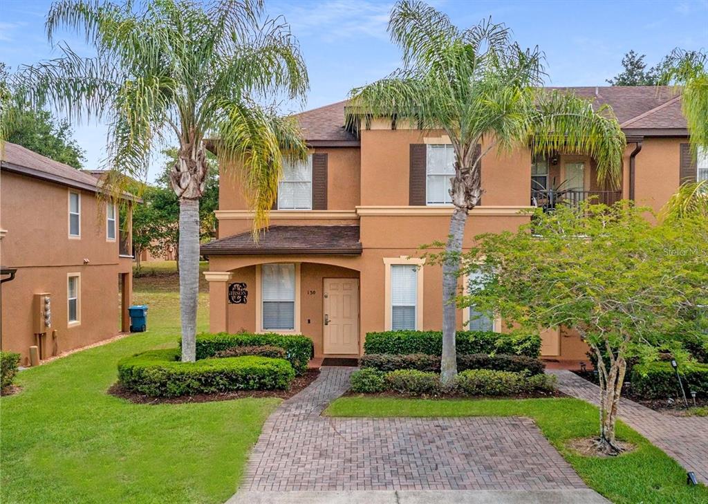 A two-story tan stucco townhouse with a brick walkway and two palm trees in front — 130 PALERMO STREET, DAVENPORT, FL