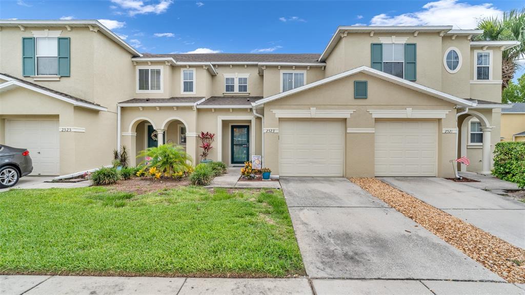 A multi-unit residential building features beige stucco walls, multiple garage doors, and green shutters — 2523 WHITE SAND LANE, CLEARWATER, FL