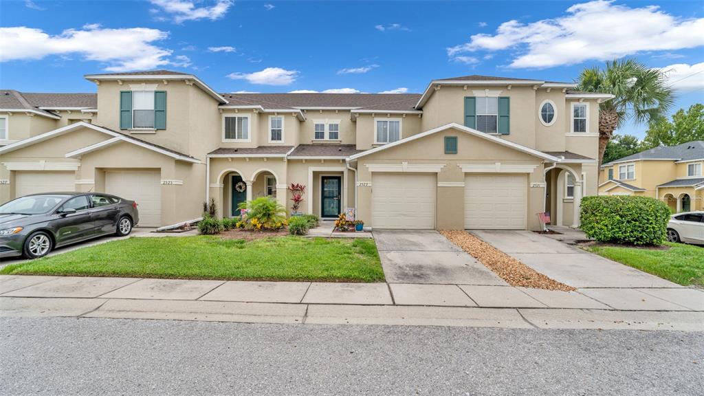 A row of two-story townhouses with beige stucco exteriors, garages, and a shared front lawn — 2523 WHITE SAND LANE, CLEARWATER, FL
