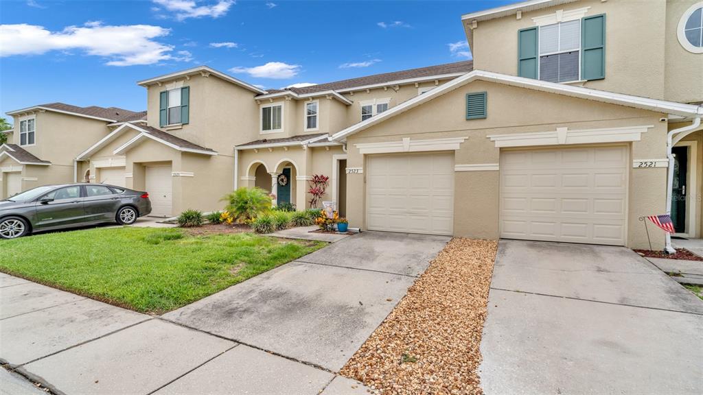 A row of beige townhouses features attached garages, concrete driveways, and green lawns — 2523 WHITE SAND LANE, CLEARWATER, FL