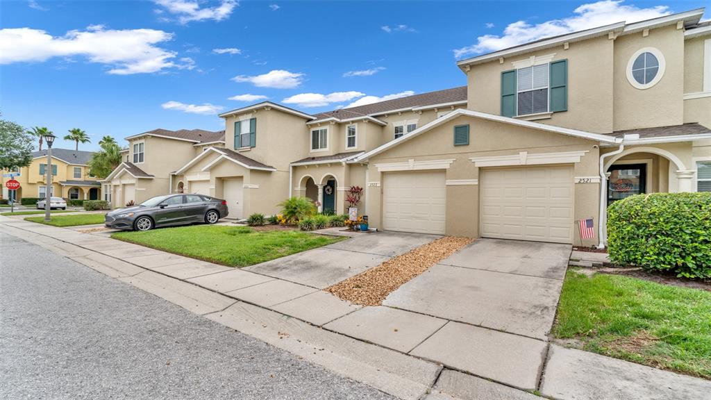 A row of two-story townhomes with beige stucco exteriors, attached garages, and concrete driveways — 2523 WHITE SAND LANE, CLEARWATER, FL